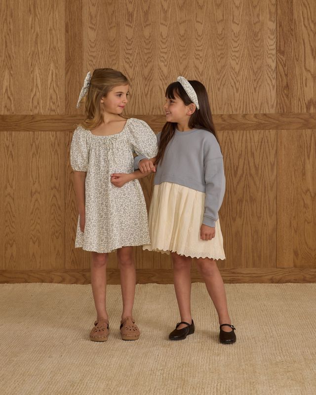 Two young girls standing against a wooden paneled wall.