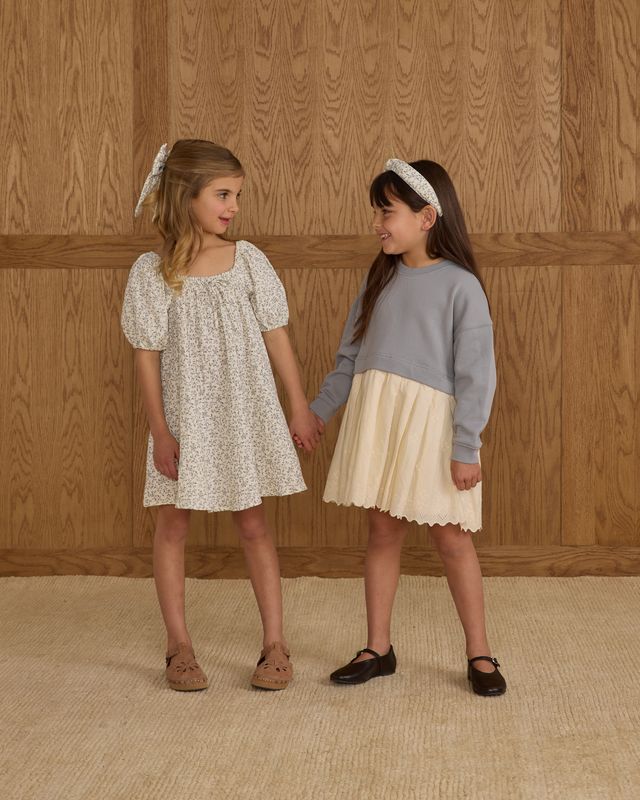 Two young girls holding hands against a wooden paneled wall.