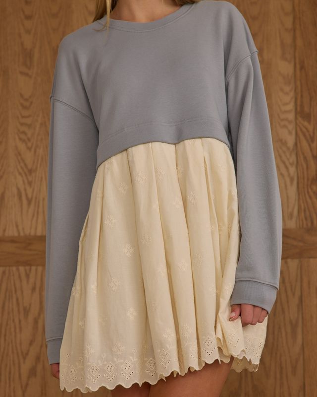 Person wearing a gray sweatshirt dress over a beige lace skirt against a wooden background