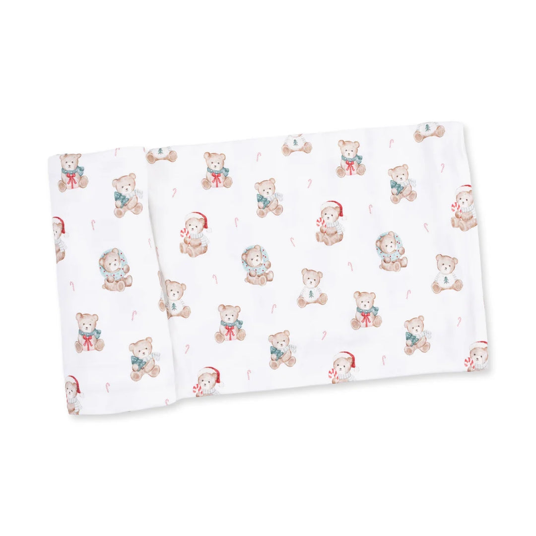 A folded white muslin blanket featuring a repeating pattern of cute teddy bears in winter clothing, including Santa hats, snowman outfits, and candy canes.