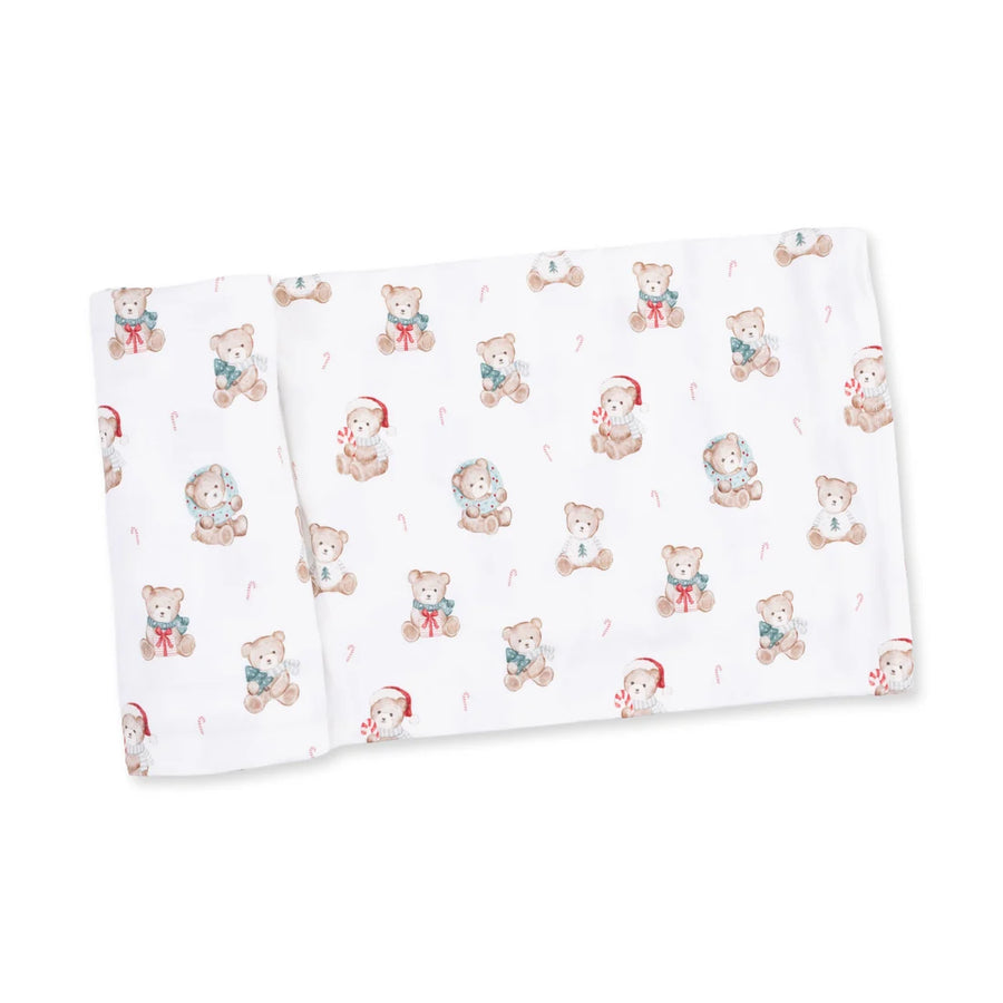 A folded white muslin blanket featuring a repeating pattern of cute teddy bears in winter clothing, including Santa hats, snowman outfits, and candy canes.