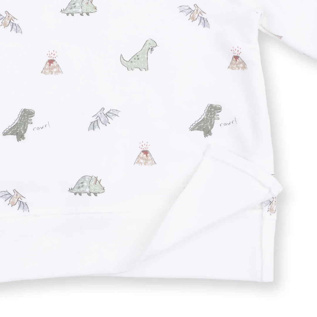 White long-sleeve baby garment with a repeating dinosaur and volcano print, shown folded with a soft corner turned over.