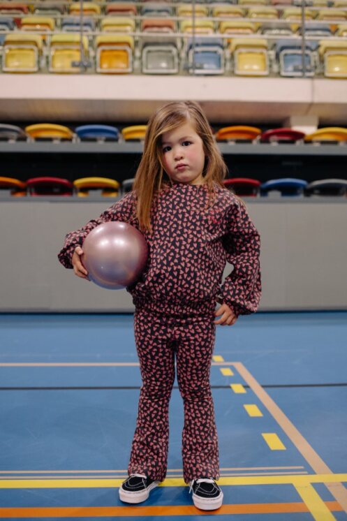 Child holding a pink ball in an indoor sports facility with colorful seats in the background.