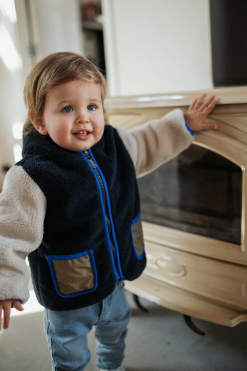 baby boy wearing a fleece jacket standing near a dresser 