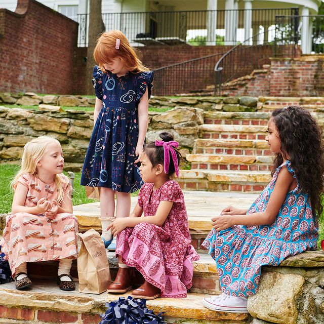 Four young girls in patterned dresses sitting on stone steps outdoors.
