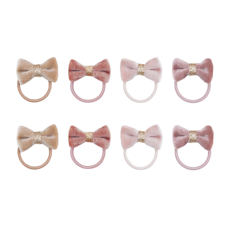 Eight velvet hair bows arranged in two rows of four on a white background. The bows come in muted shades of beige, dusty pink, blush, and mauve, each with a glittery gold center band and a matching elastic loop.