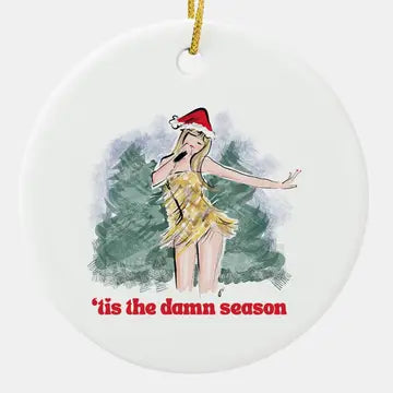 Taylor swift christmas ornament, she is dressed in a gold sequin outfit and santa hat in front of Christmas trees. 