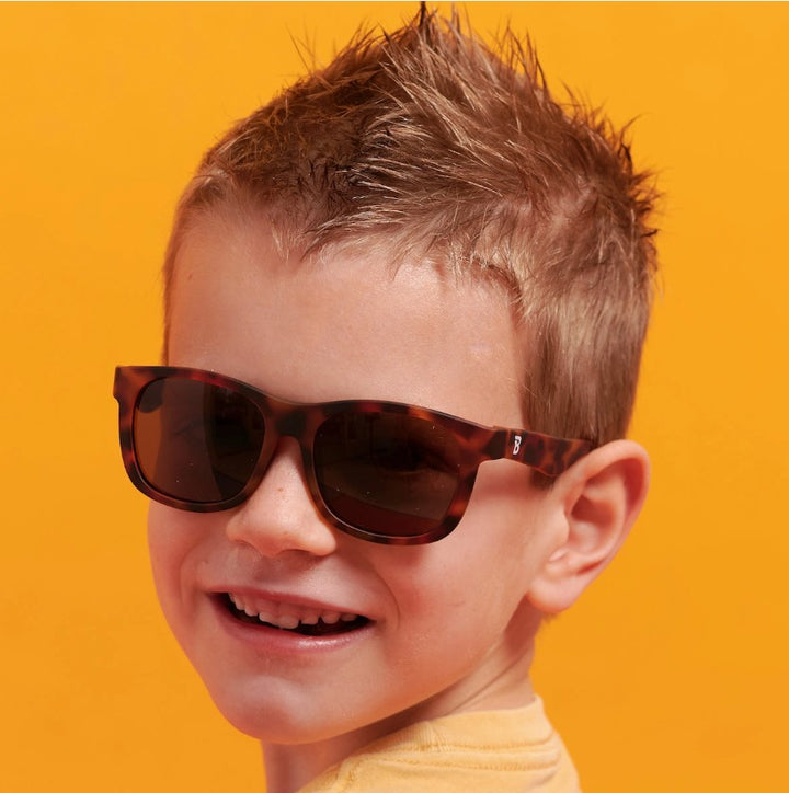 Child wearing tortoiseshell sunglasses against an orange background