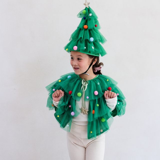 Child wearing a festive green Christmas tree costume with colorful decorations on a plain background