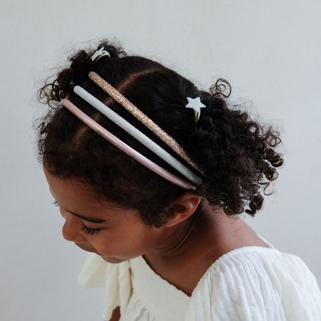 Child wearing pastel glitter headbands with star accessories on a plain background