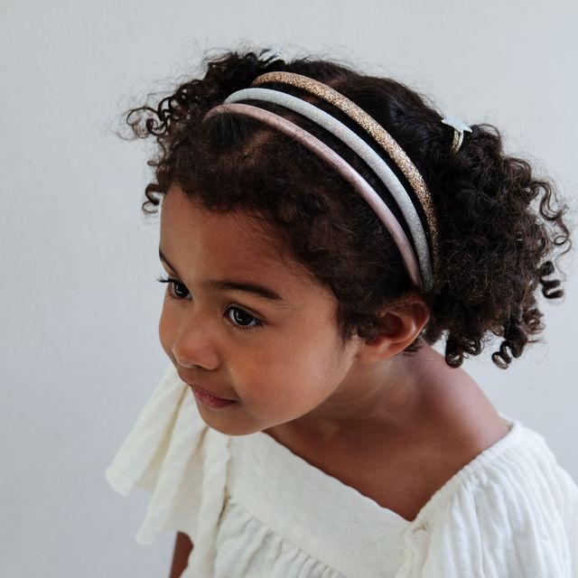Young girl wearing a headband with multiple glitter headbands against a plain background