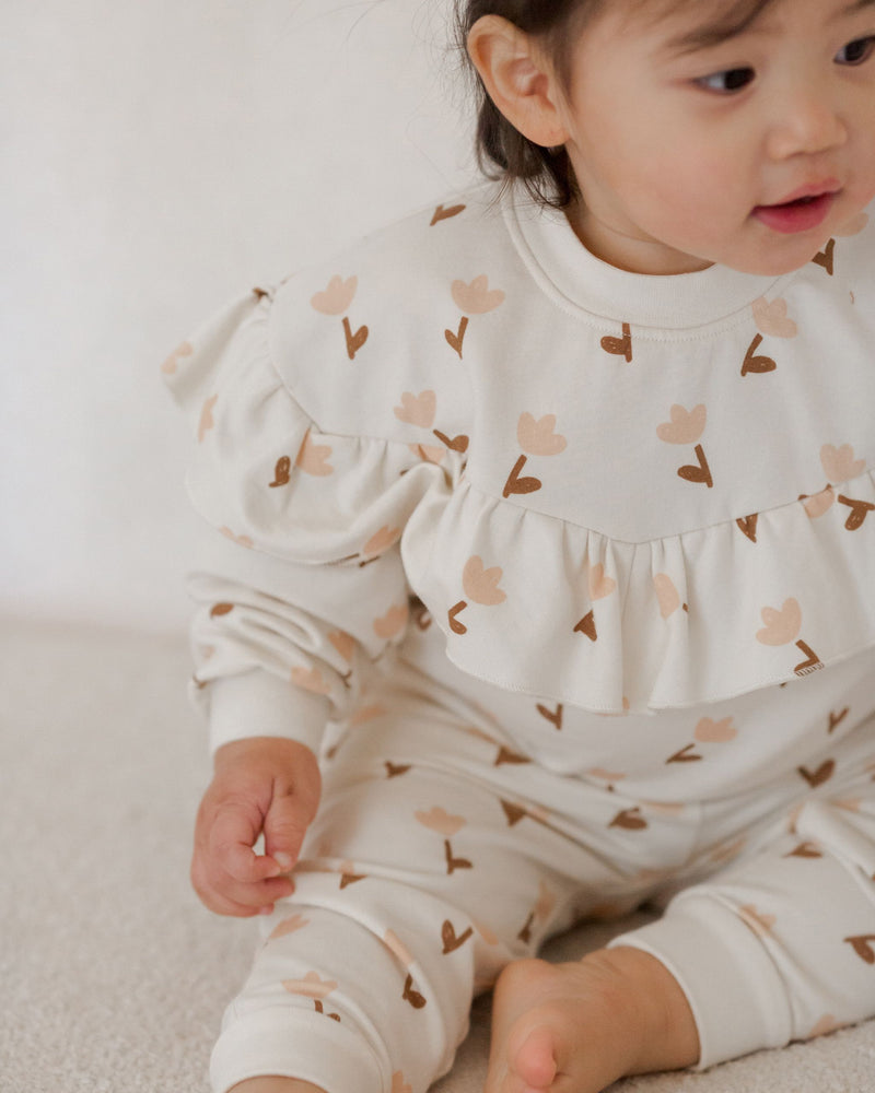 Picture of a toddler wearing the all over tulip print sweat set. the toddler is sitting down showing the drama the ruffle creates.  