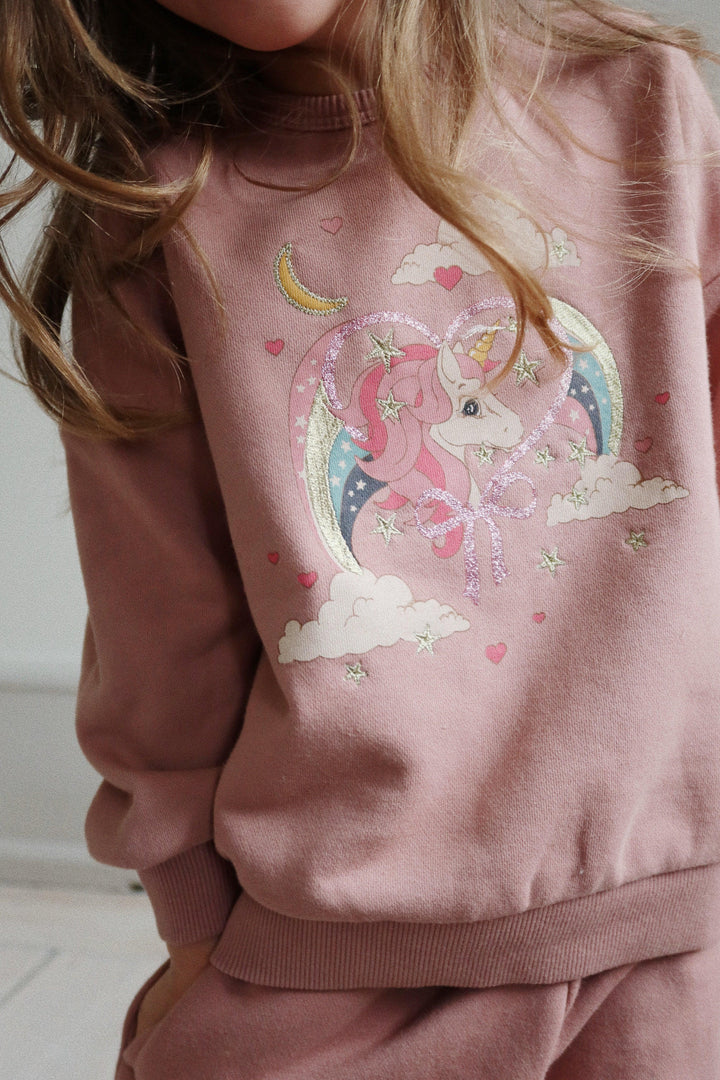 a close up image of the unicorn print on the sweatshirt. The unicorn is in the center of a heart with rainbows surrounding it and clouds on the top and bottom. 