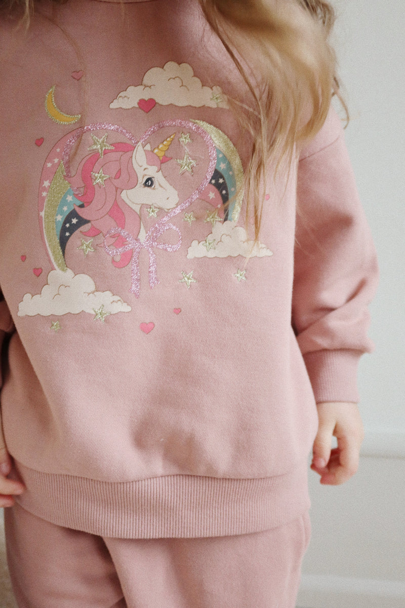 a full shot of the unicorn sweatshirt on a young girl modeling it. The sweatshirt has a roomy fit, pastel color palette. 