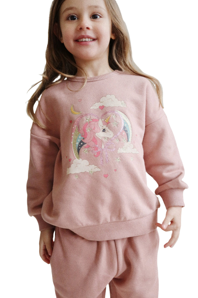 full shot of a young girl wearing the sweatshirt with sweatpants. The sweatshirt is a dusty rose color with a unicorn on the front. 