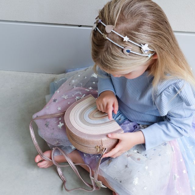 Young girl in a blue dress with star headband holding a pink and beige handbag.