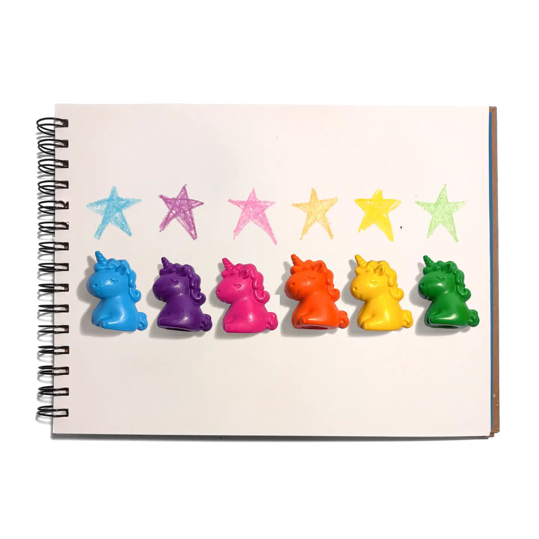 Six small unicorn-shaped crayons in blue, purple, pink, orange, yellow, and green are lined up on a white spiral notebook page below six colored star crayons.