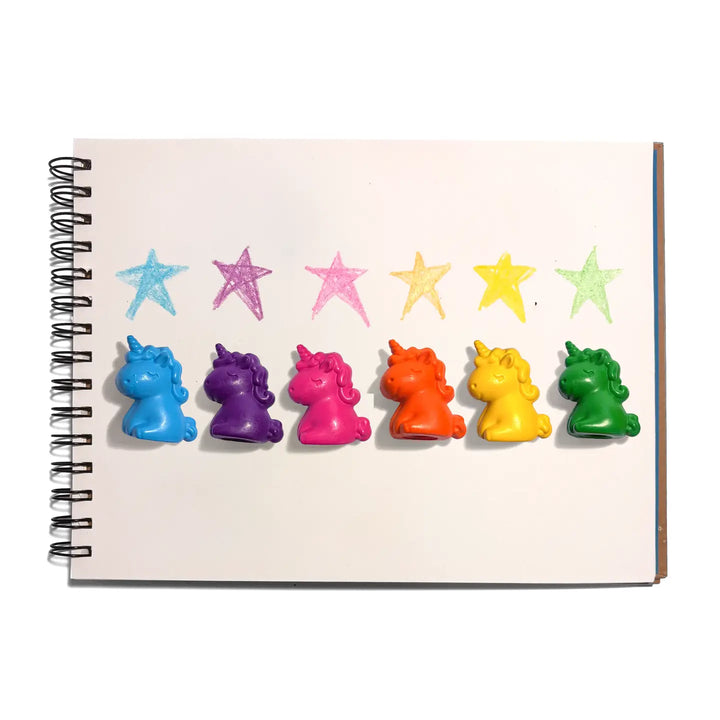 Six small unicorn-shaped crayons in blue, purple, pink, orange, yellow, and green are lined up on a white spiral notebook page below six colored star crayons.