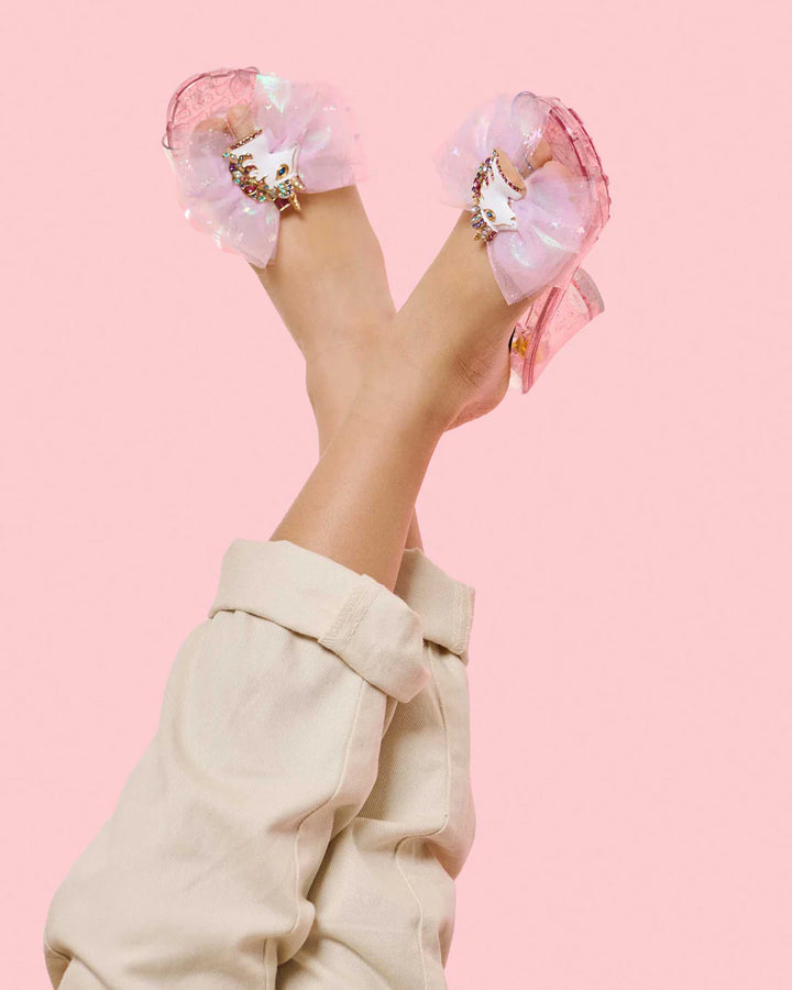 a young girl modeling the pink slip on shoes with a pink tulle bow and an enamel unicorn clip