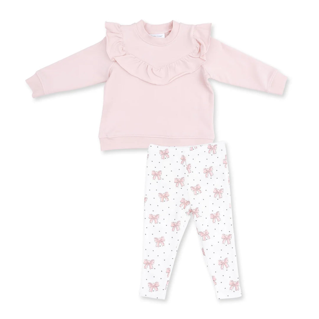 A toddler girl's two-piece clothing set featuring a light pink long-sleeve top with a ruffled collar and white leggings with a pink bow and polka dot pattern, laid flat on a white background.