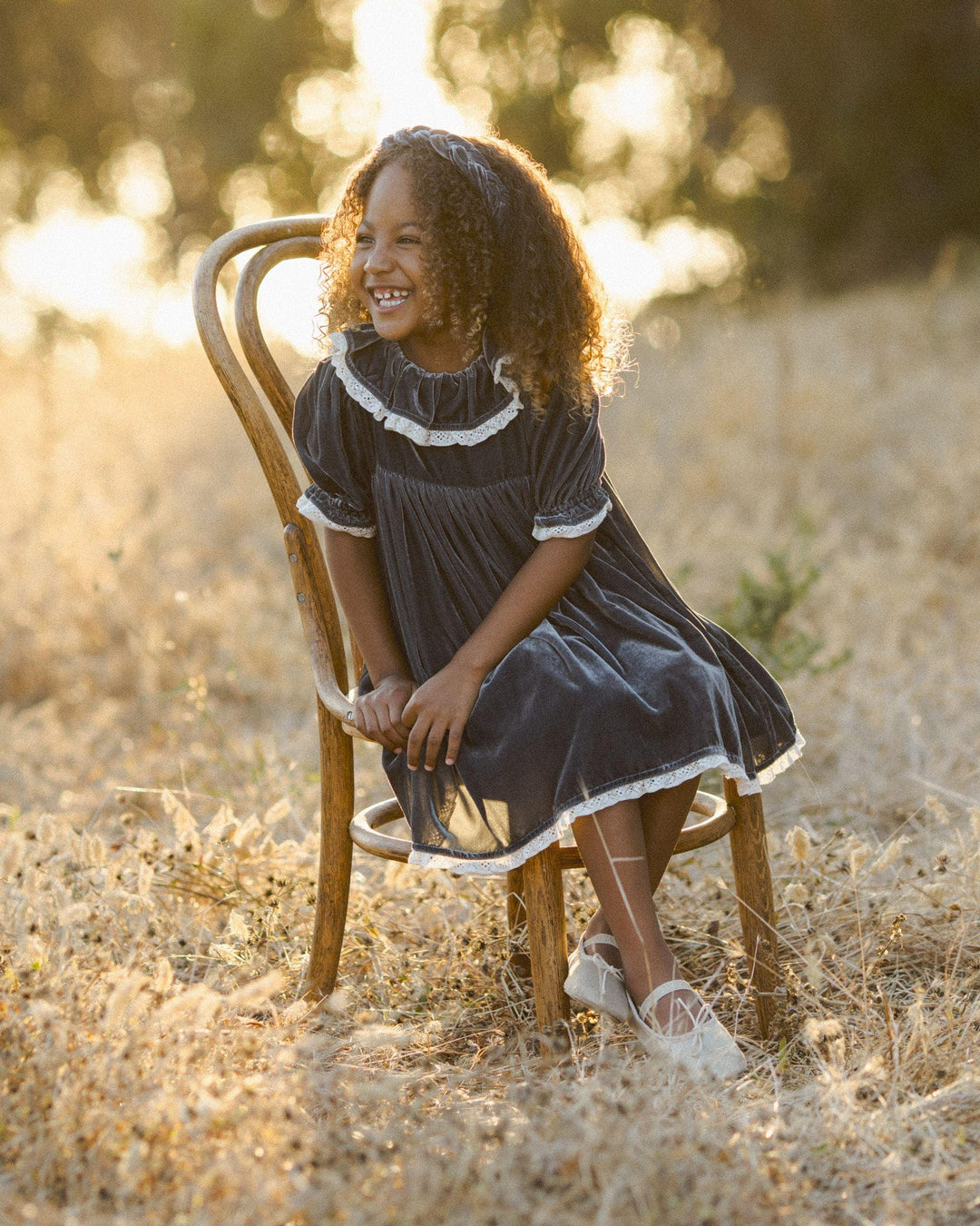 little girl modeling the gray velvet dress while sitting in a chair in the beautiful afternoon light. 