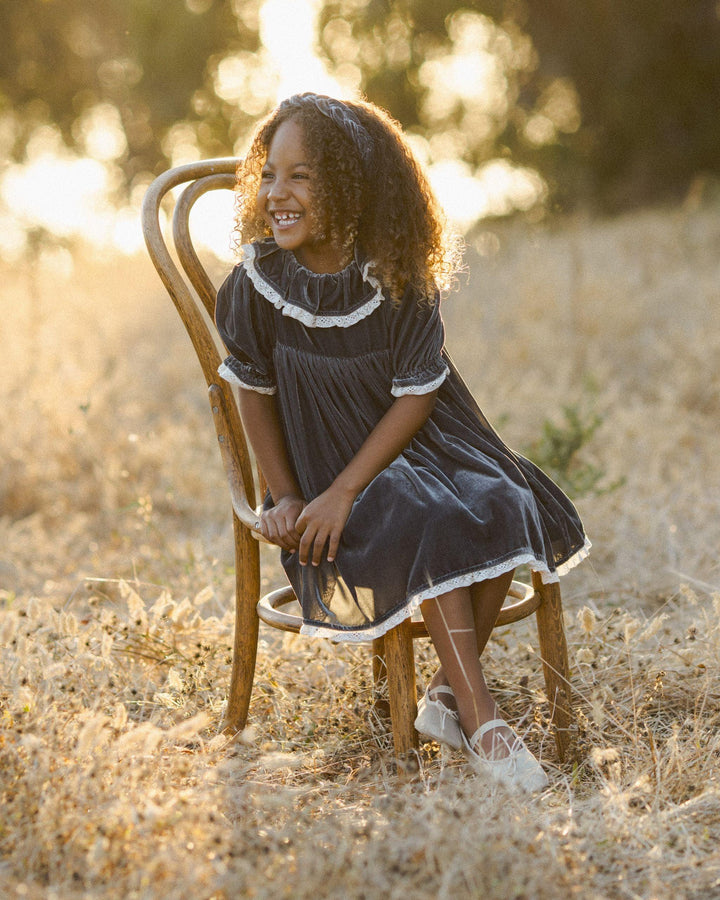 little girl modeling the gray velvet dress while sitting in a chair in the beautiful afternoon light. 