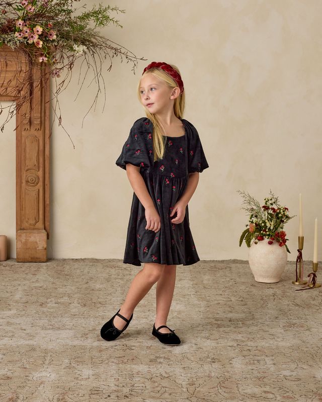 Young girl in a black floral dress standing in a room with decorative elements.