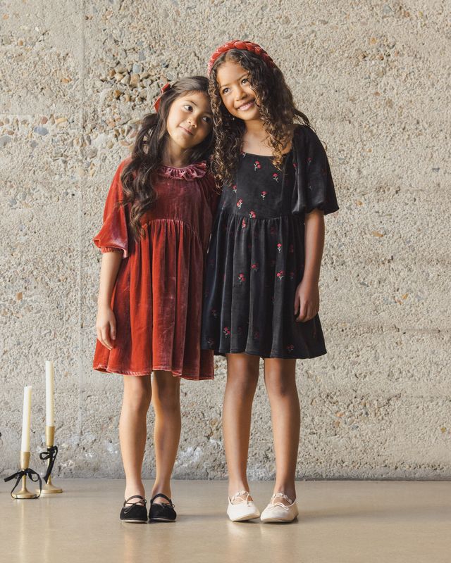 Two young girls in red and black dresses standing against a textured wall.