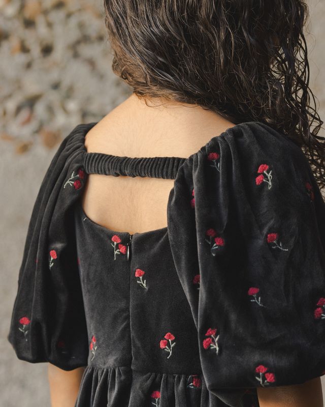 Black dress with floral embroidery on a textured wall background