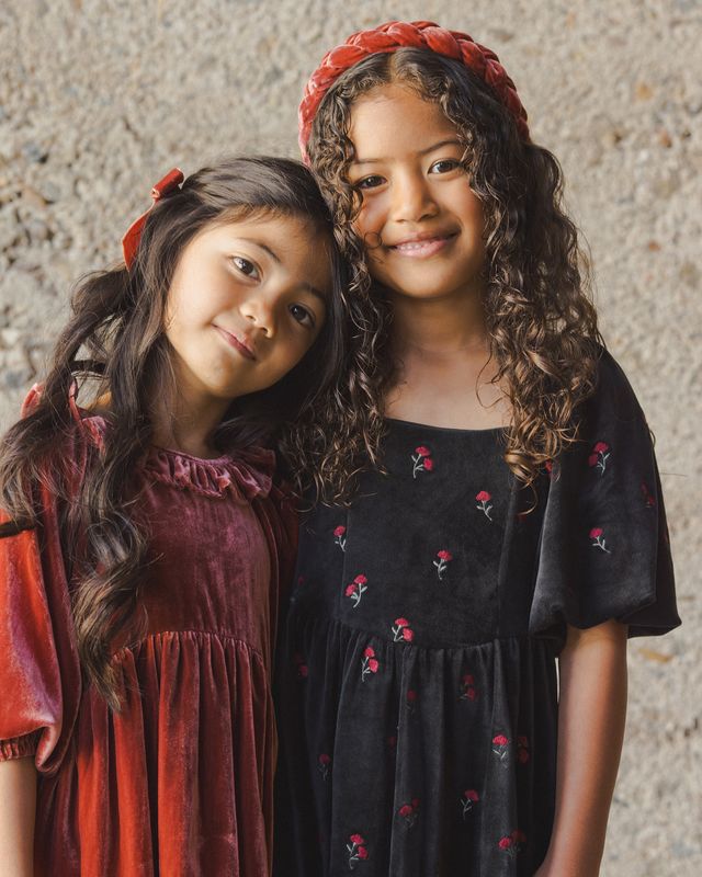 Two young girls wearing dresses with floral patterns against a textured wall.