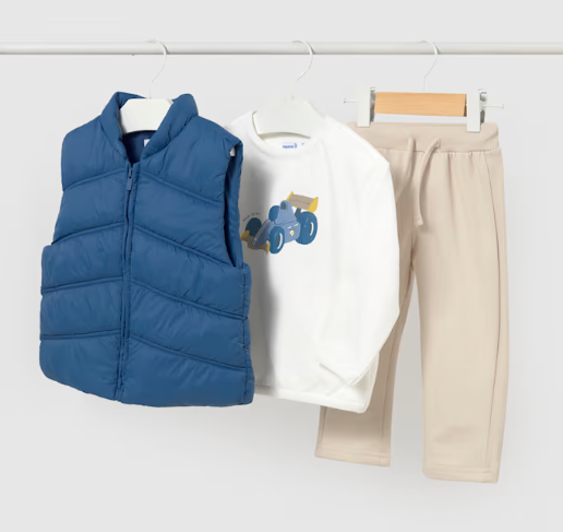 A children's three-piece outfit set hanging on white hangers against a light gray background. The set includes a royal blue quilted zip-front puffer vest, a white long-sleeve shirt with a blue and yellow tractor graphic, and beige drawstring sweatpants.