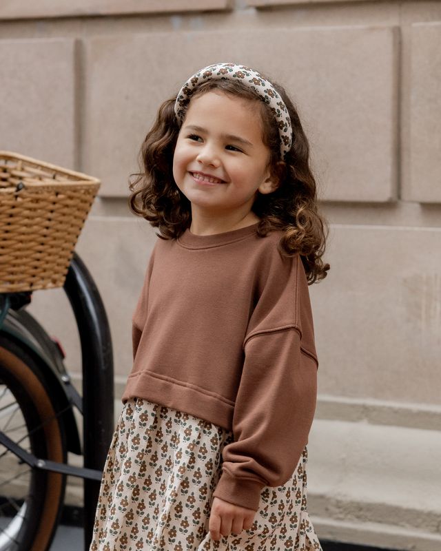 Young girl wearing a brown sweater and floral skirt with a bike in the background