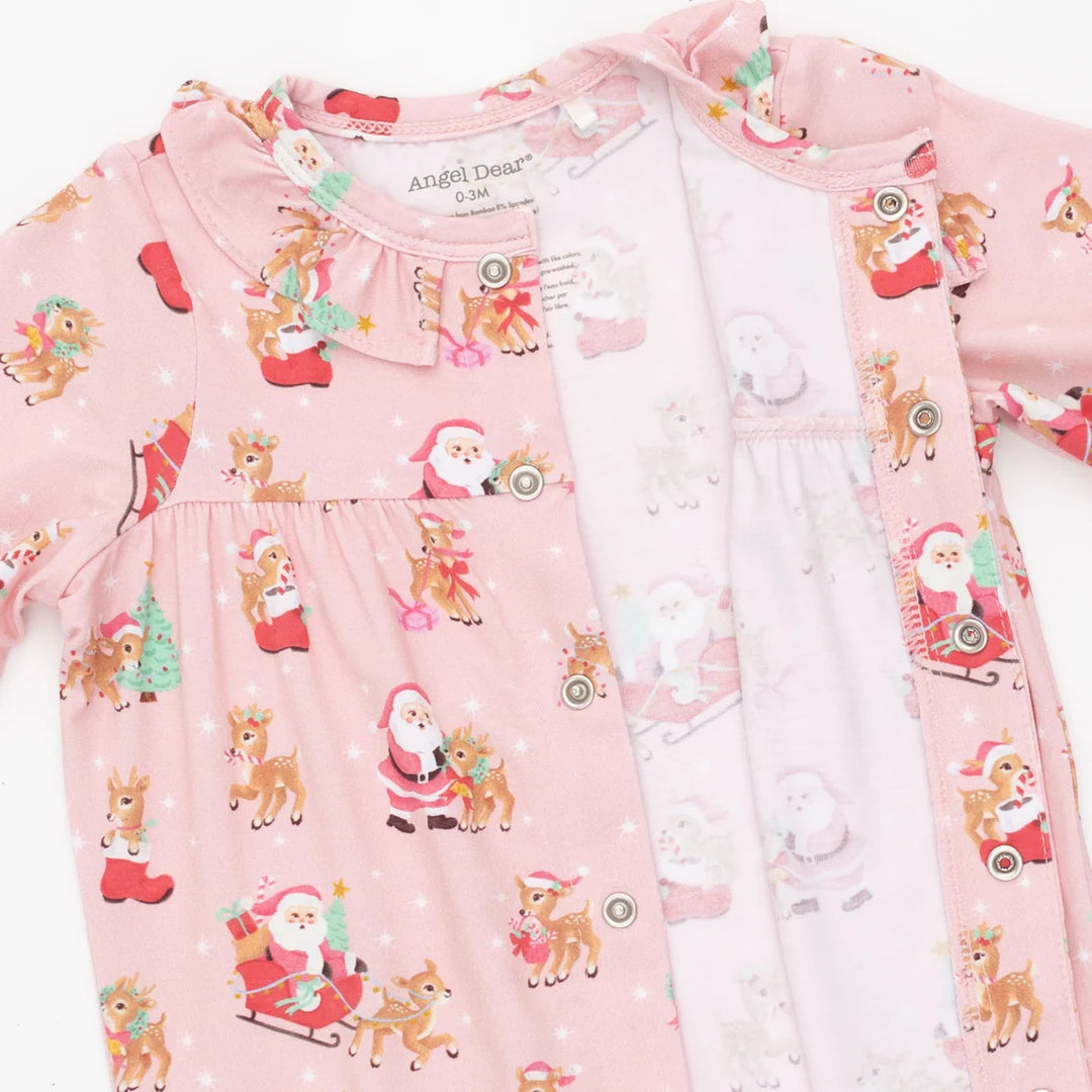 A baby girl's pink long-sleeve sleep suit featuring a festive Christmas print with Santa Claus, reindeer, and snowman motifs. The garment has a ruffled collar, snap-button front, and a matching inner hood.