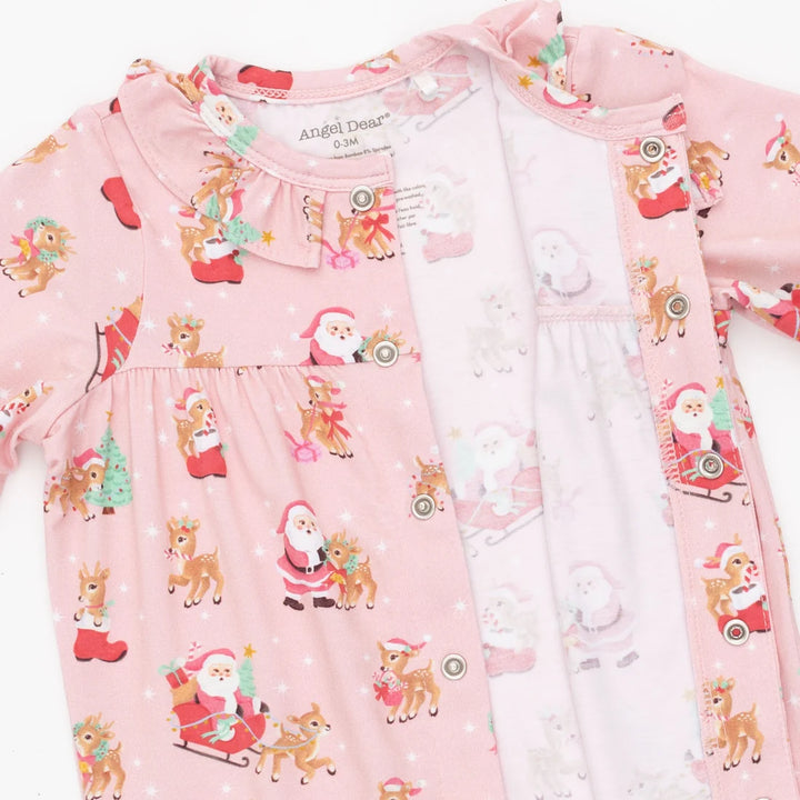 A baby girl's pink long-sleeve sleep suit featuring a festive Christmas print with Santa Claus, reindeer, and snowman motifs. The garment has a ruffled collar, snap-button front, and a matching inner hood.