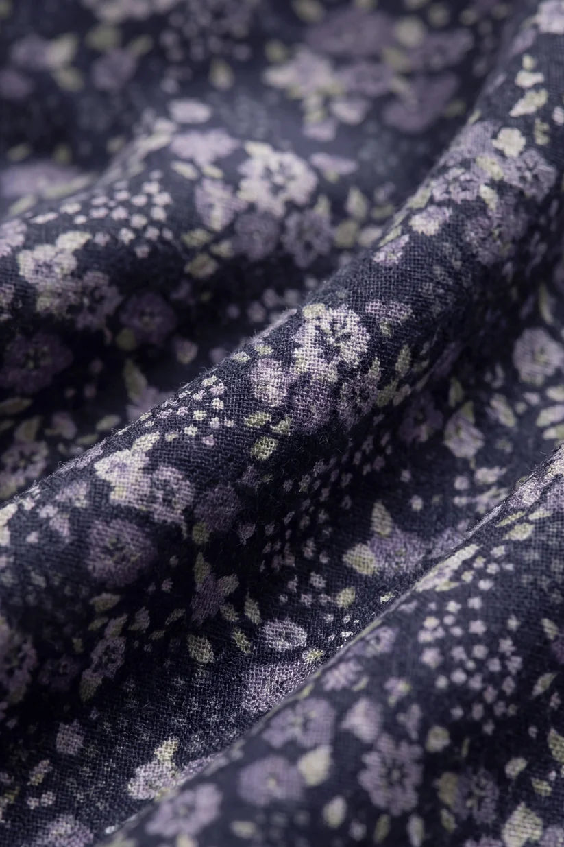 A close-up of draped fabric with a dark navy or black base and an allover floral print in lavender, purple, and pale green.