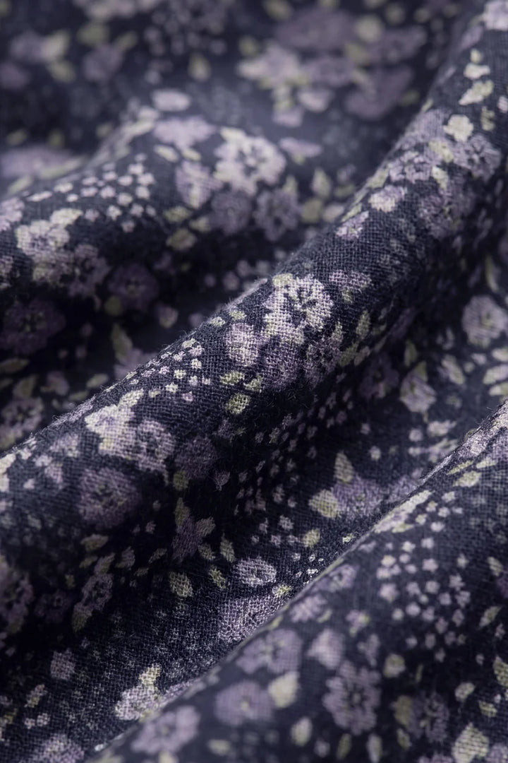A close-up of draped fabric with a dark navy or black base and an allover floral print in lavender, purple, and pale green.