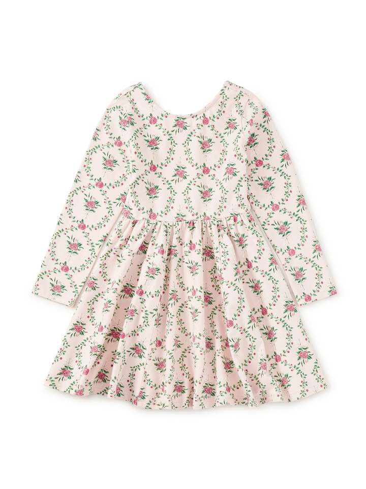 A long-sleeve children's dress with a gathered waist and a delicate pink and green floral print on a light cream background, shown flat against a white background.