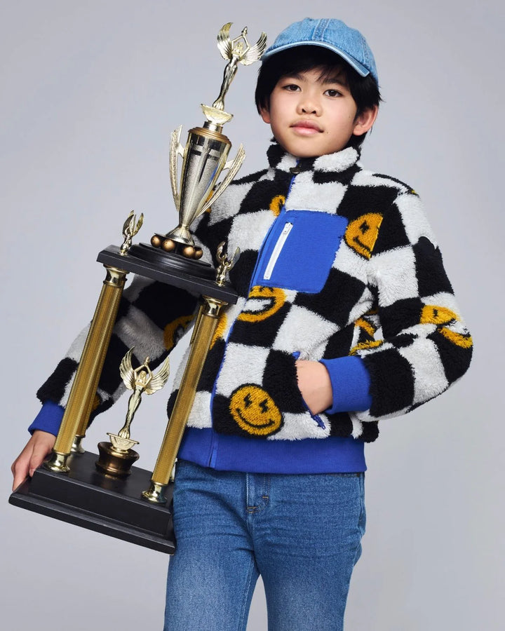 young boy wearing the black and white checkered sherpa holding a trophy. 