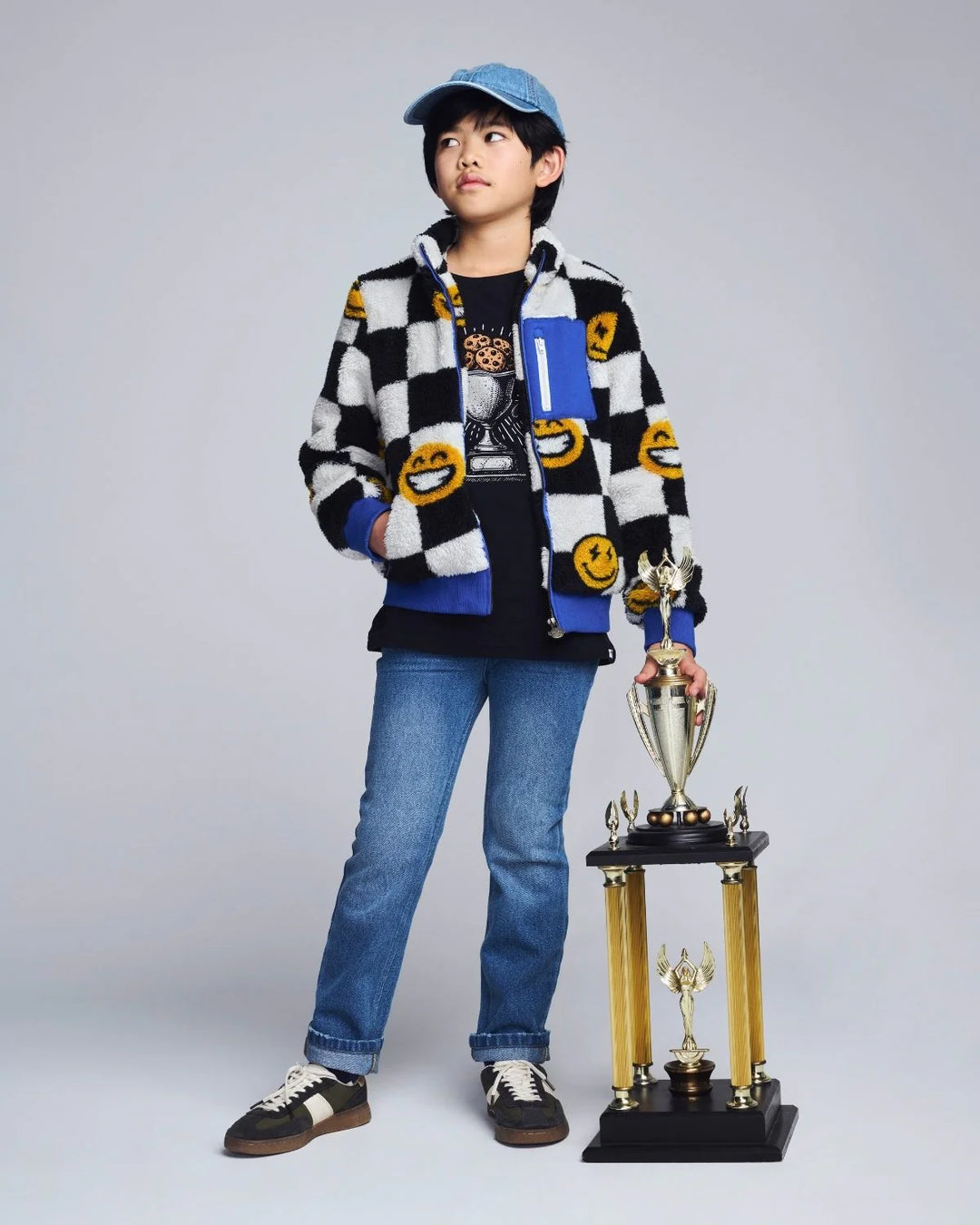 young boy wearing a black and white check sherpa with yellow smiley faces all over and blue accents on the jacket. 