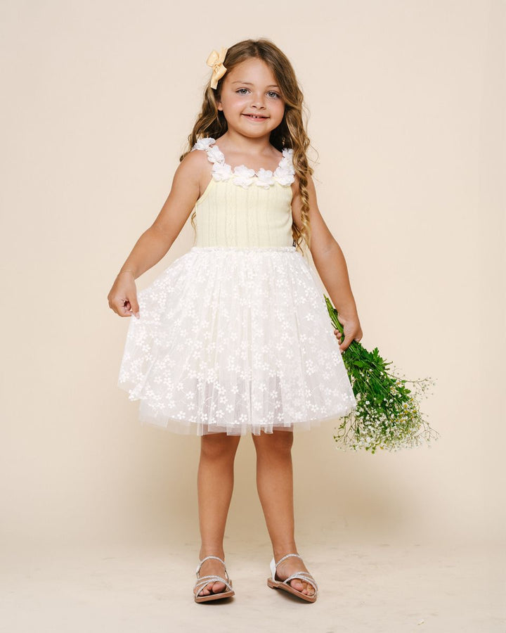 Young girl in a white and yellow dress holding flowers against a beige background
