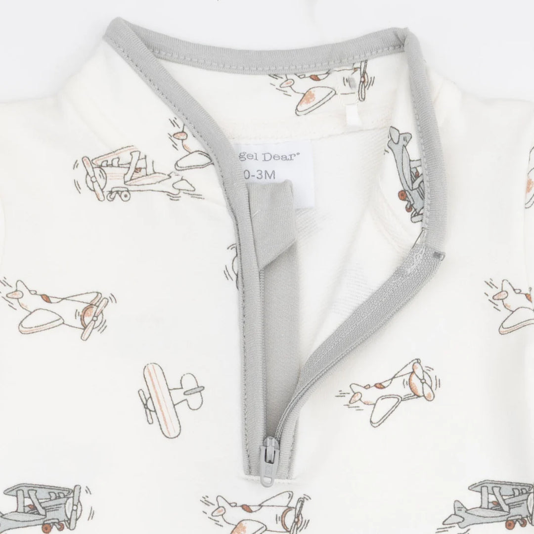 Close-up of a baby garment with a light gray zipper and trim, featuring an off-white fabric printed with small vintage airplane illustrations. The brand name 'Goi Deer' is visible on the inner neck label.