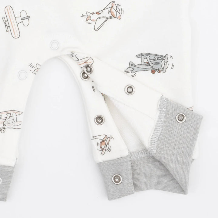 Close-up of a baby romper or long-sleeve top in white fabric with a light gray and orange airplane print, featuring gray ribbed cuffs and snap closures.